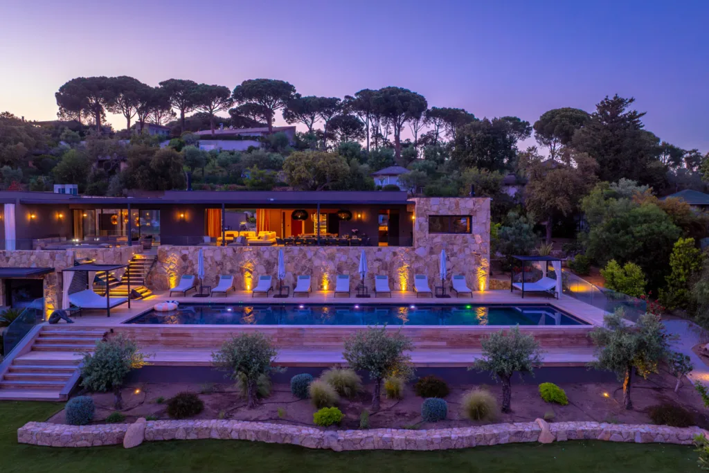 L'Hôtel Villa Padulaccia et sa piscine éclairés au crépuscule, pins parasols sur un ciel mauve