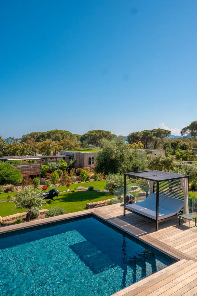 Lit de repos sous pergola au bord de la piscine chauffée de l'Hôtel Villa Padulaccia, jardin et pins en contrebas